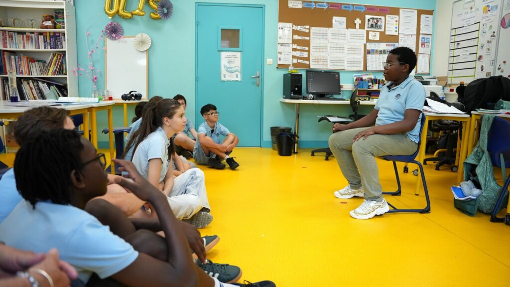 Des collégiens assis au sol écoutent un adulte lors d’un temps d’échange en classe