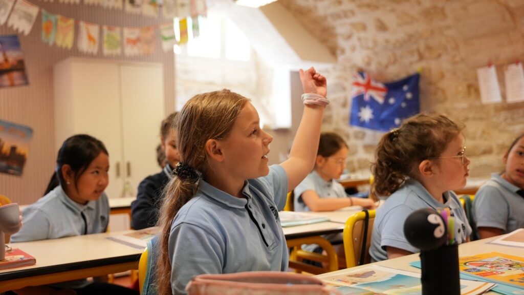 Des écoliers lèvent la main dans une classe de la section anglophone, drapeaux au mur
