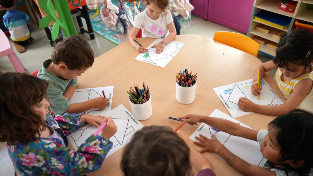 Des enfants de maternelle dessinent autour d’une table d’atelier